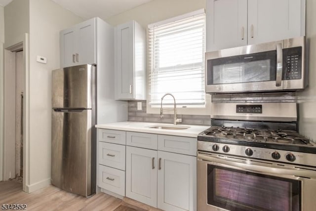 kitchen with light countertops, light wood-style flooring, decorative backsplash, appliances with stainless steel finishes, and a sink