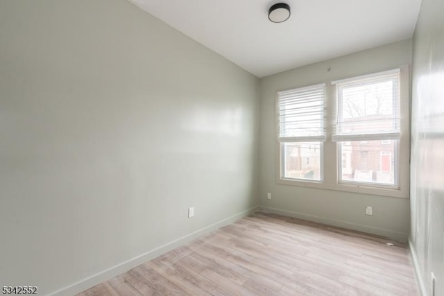 empty room featuring light wood-style floors, lofted ceiling, and baseboards