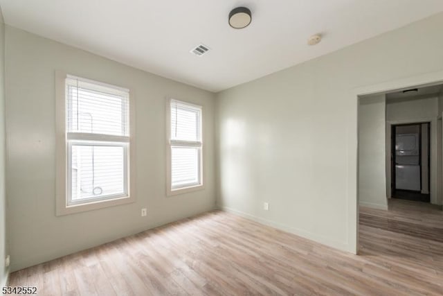 unfurnished room featuring light wood finished floors, visible vents, and baseboards