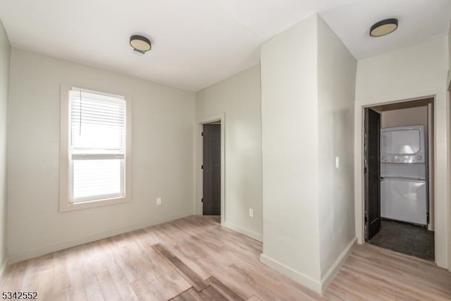 empty room with stacked washing maching and dryer, light wood-style flooring, and baseboards