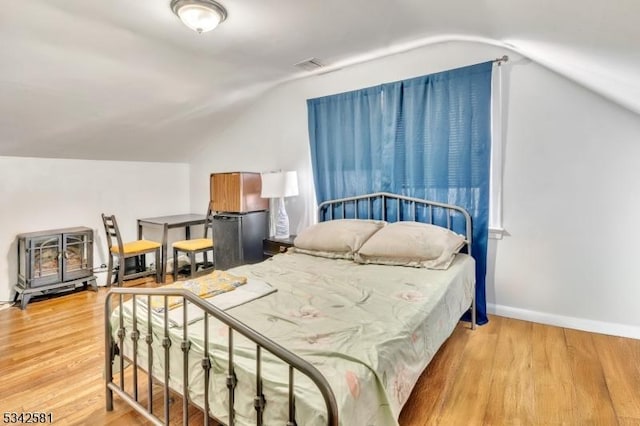 bedroom with lofted ceiling, visible vents, freestanding refrigerator, a wood stove, and light wood-type flooring