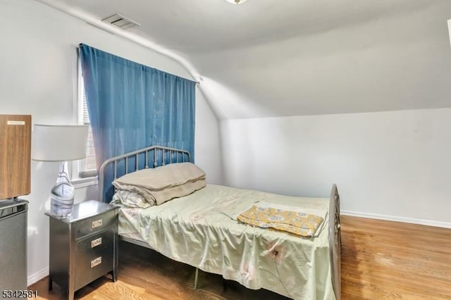 bedroom with lofted ceiling, visible vents, baseboards, and wood finished floors