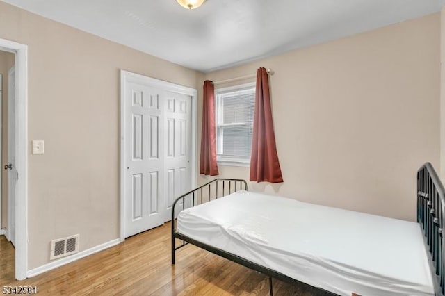 bedroom featuring light wood finished floors, baseboards, visible vents, and a closet