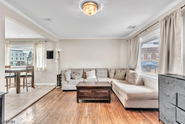 living area featuring baseboards, visible vents, crown molding, and light wood finished floors