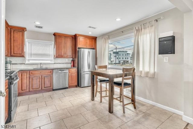 kitchen with tasteful backsplash, baseboards, brown cabinetry, appliances with stainless steel finishes, and a sink