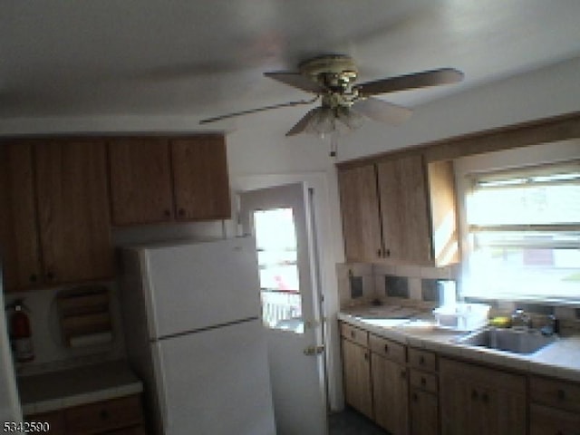 kitchen with a ceiling fan, tile countertops, freestanding refrigerator, a sink, and backsplash