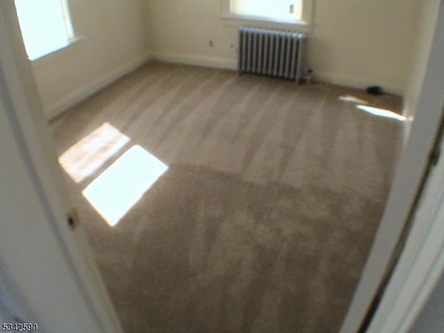 empty room with baseboards, light wood finished floors, and radiator