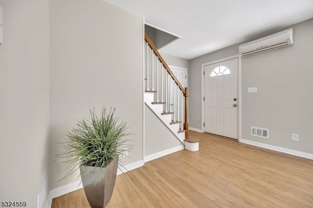 foyer entrance featuring visible vents, stairway, light wood-style floors, an AC wall unit, and baseboards