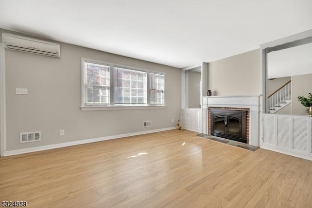 unfurnished living room with baseboards, visible vents, light wood-type flooring, a fireplace, and a wall mounted AC