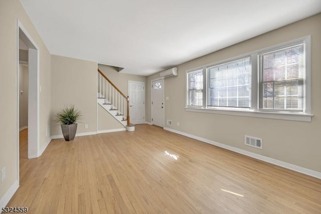 foyer entrance featuring light wood-type flooring, baseboards, a wall unit AC, and stairway