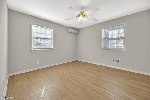 empty room featuring a wealth of natural light, a wall unit AC, visible vents, and baseboards