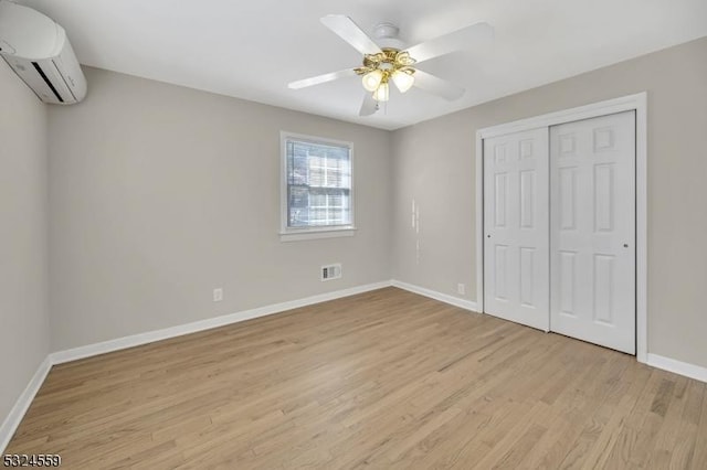 unfurnished bedroom featuring baseboards, visible vents, light wood-style flooring, an AC wall unit, and a closet