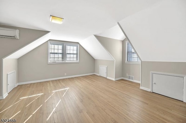 bonus room featuring baseboards, wood finished floors, a wealth of natural light, and a wall mounted air conditioner