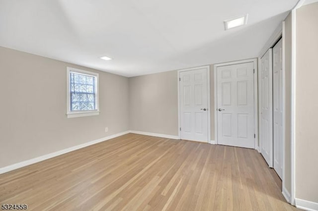 unfurnished bedroom featuring light wood-type flooring, baseboards, and two closets