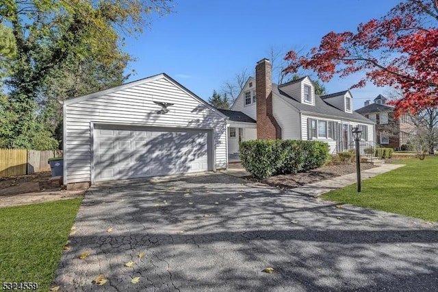 cape cod house with aphalt driveway, a chimney, fence, a garage, and a front lawn