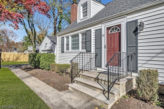 property entrance featuring a shingled roof, a chimney, and fence