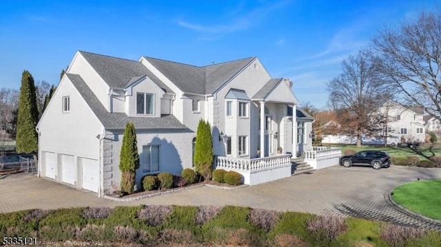 view of side of home featuring driveway, a porch, an attached garage, and a shingled roof