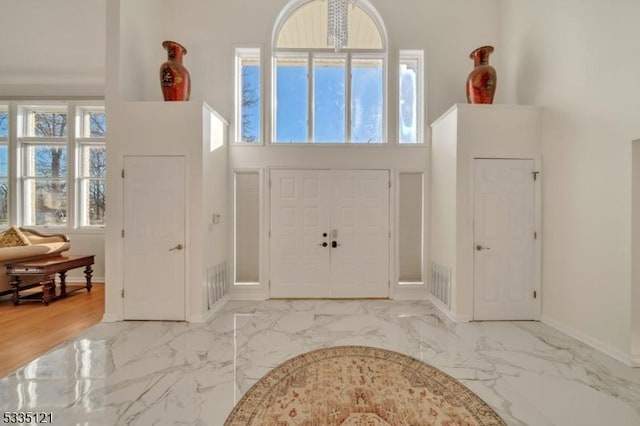 foyer entrance featuring marble finish floor, visible vents, a high ceiling, and baseboards