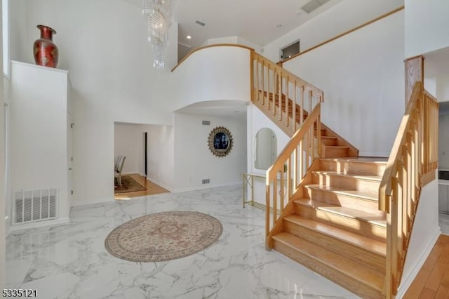 foyer entrance featuring marble finish floor, visible vents, a towering ceiling, baseboards, and stairs