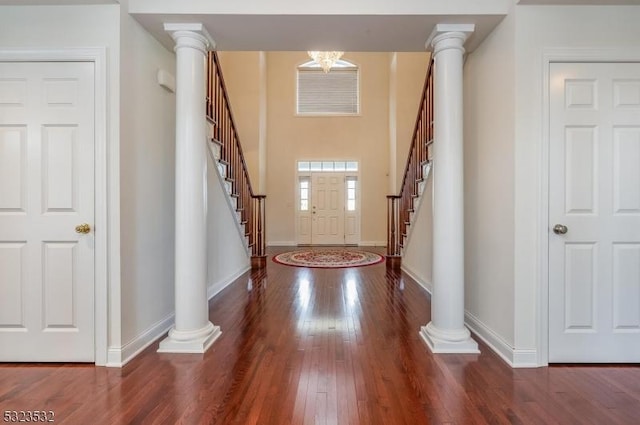 entrance foyer with decorative columns, stairway, wood-type flooring, and baseboards