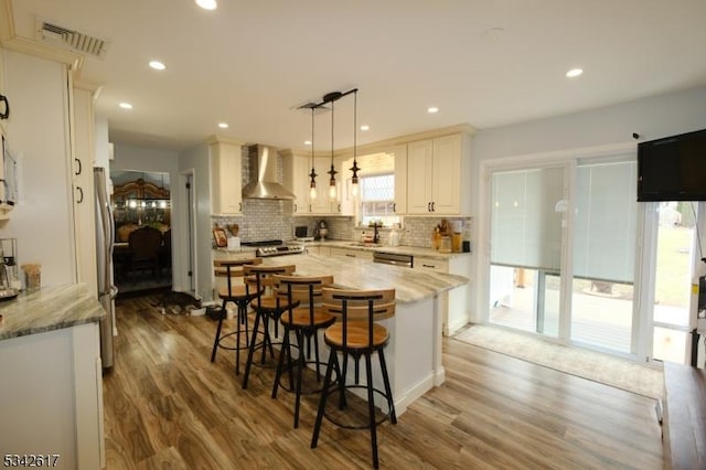 kitchen with stainless steel appliances, a breakfast bar, visible vents, wall chimney range hood, and backsplash