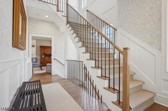 staircase featuring a wainscoted wall, wood finished floors, a towering ceiling, and a decorative wall