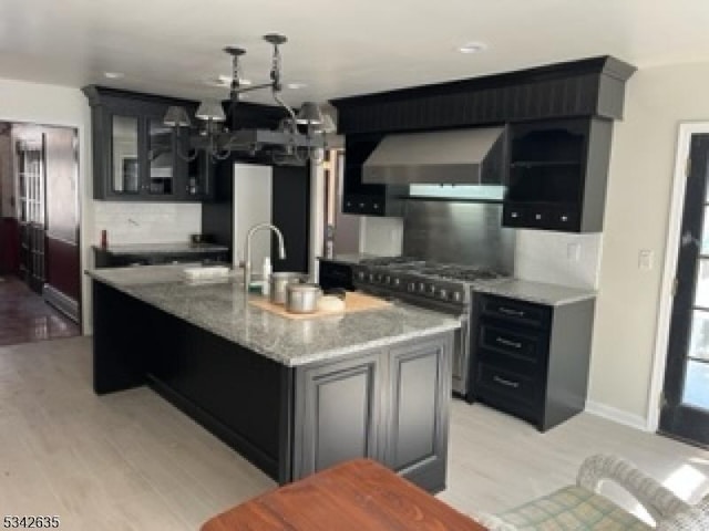 kitchen with wall chimney range hood, glass insert cabinets, backsplash, and high end stainless steel range