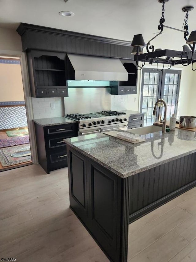 kitchen with light stone counters, double oven range, open shelves, wall chimney range hood, and light wood-type flooring