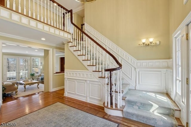 entrance foyer featuring a decorative wall, ornamental molding, a towering ceiling, and wood finished floors