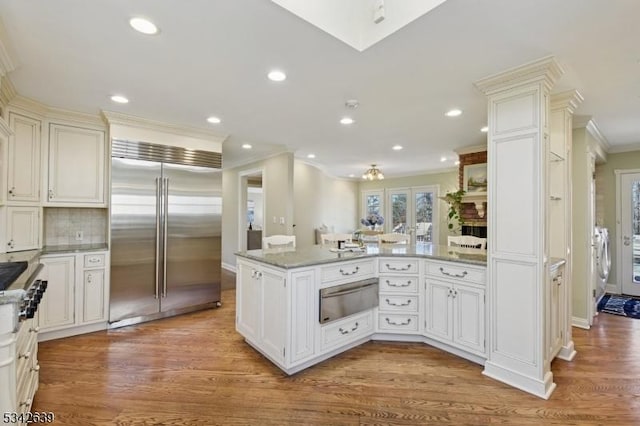 kitchen with a warming drawer, stainless steel built in fridge, ornamental molding, wood finished floors, and a peninsula