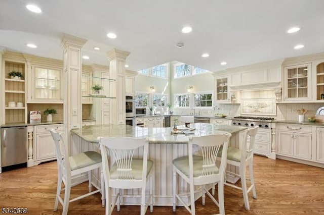 kitchen with glass insert cabinets, light stone countertops, light wood-style floors, and appliances with stainless steel finishes