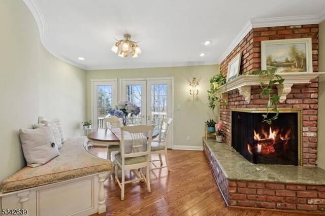 dining space featuring baseboards, recessed lighting, ornamental molding, a brick fireplace, and light wood-type flooring