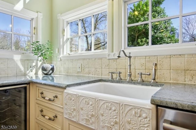 kitchen with a sink, wine cooler, tasteful backsplash, and light stone counters