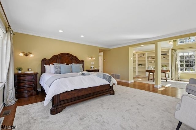 bedroom with visible vents, baseboards, wood finished floors, and crown molding