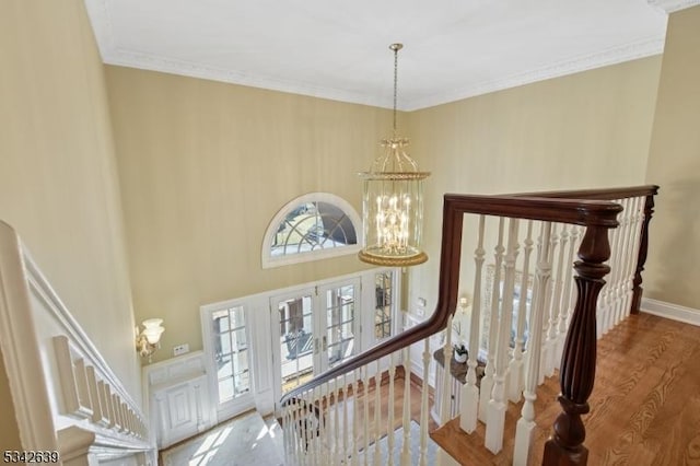 stairs featuring a chandelier, ornamental molding, baseboards, and wood finished floors