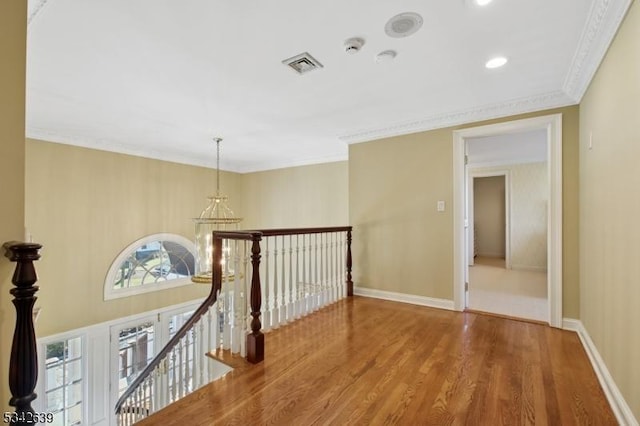 hall with visible vents, baseboards, ornamental molding, an upstairs landing, and wood finished floors