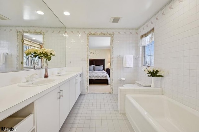 ensuite bathroom with a sink, a tub to relax in, tile walls, and tile patterned floors