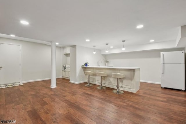 kitchen with dark wood-type flooring, freestanding refrigerator, recessed lighting, a peninsula, and a breakfast bar area