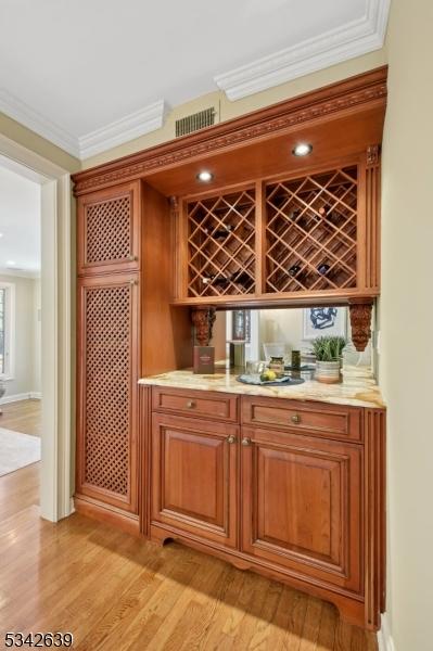 bar featuring a bar, crown molding, and light wood-style flooring