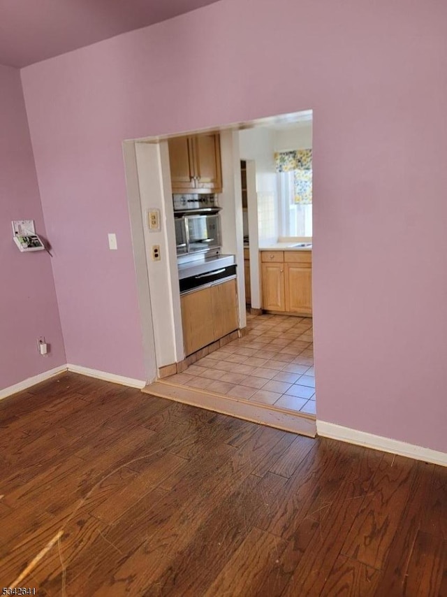 kitchen featuring baseboards, light brown cabinetry, oven, and light wood-style floors