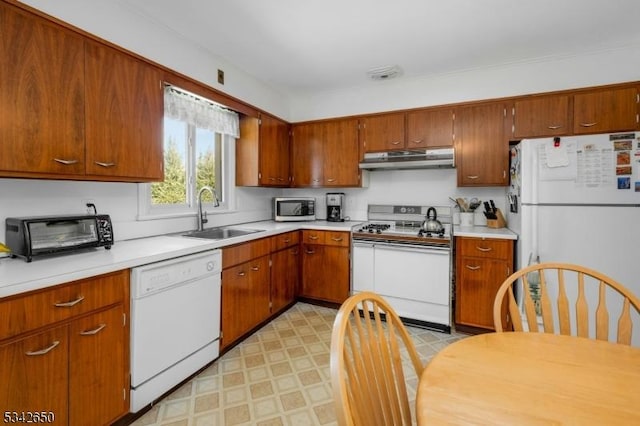 kitchen featuring under cabinet range hood, white appliances, a sink, light countertops, and light floors