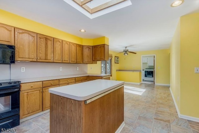 kitchen with a skylight, light countertops, a center island, black appliances, and brown cabinetry