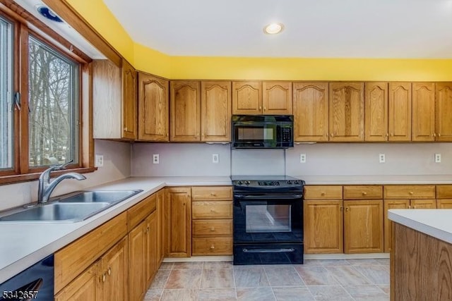 kitchen featuring black appliances, brown cabinetry, a sink, and light countertops