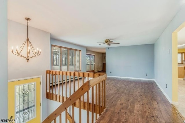 hall featuring baseboard heating, an inviting chandelier, an upstairs landing, wood finished floors, and baseboards