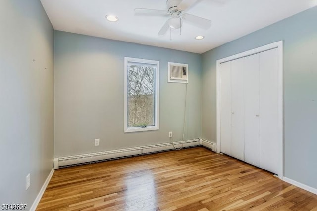 unfurnished bedroom with a baseboard radiator, a closet, recessed lighting, a wall mounted AC, and light wood-style floors