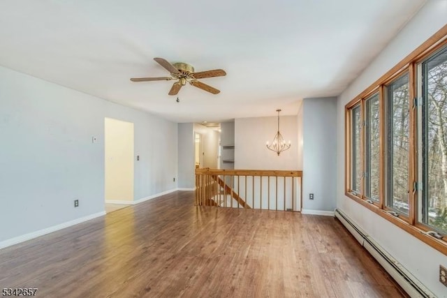 spare room with ceiling fan with notable chandelier, a baseboard radiator, wood finished floors, and baseboards