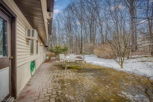 snow covered patio featuring a wall unit AC and outdoor dining space