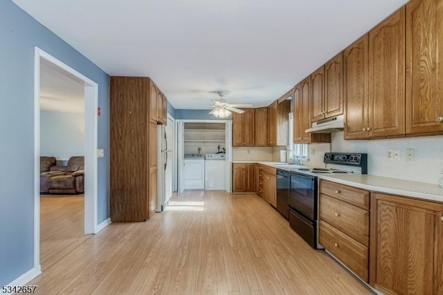 kitchen with electric stove, washer and clothes dryer, brown cabinetry, a sink, and under cabinet range hood