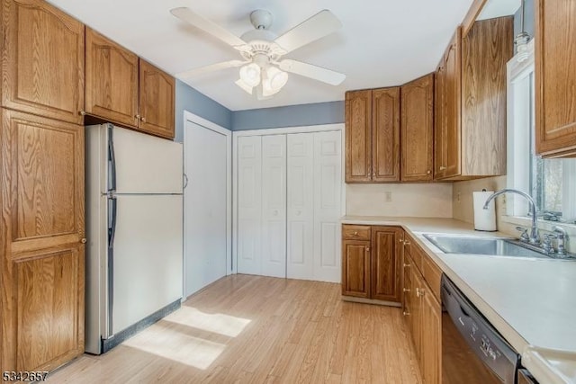 kitchen with dishwasher, brown cabinetry, a sink, and freestanding refrigerator