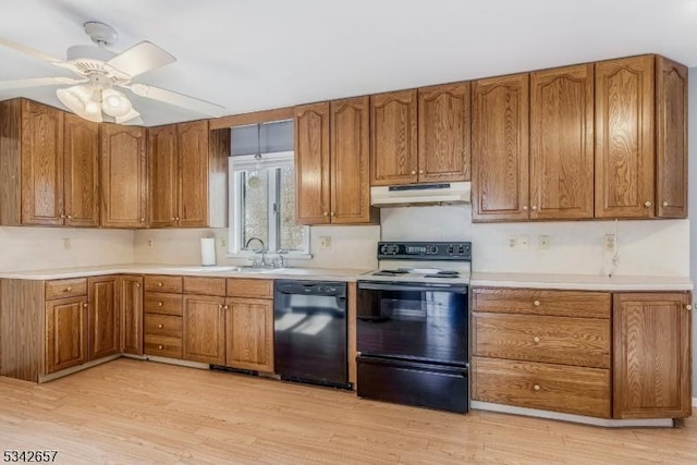 kitchen featuring brown cabinetry, a sink, under cabinet range hood, and black appliances